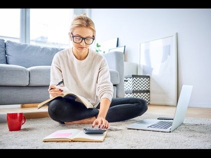 Woman sitting on the floor working on her computer and calculator. 