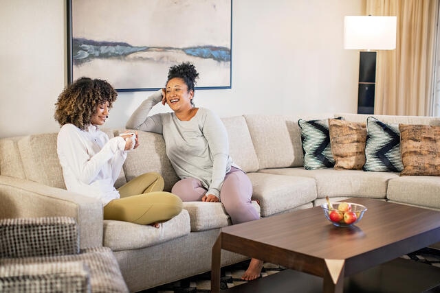 An older woman and younger woman sitting together on a couch in a Hilton Grand Vacations suite. 