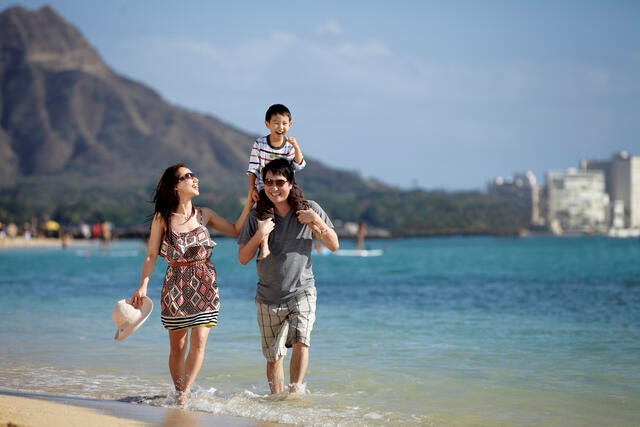 Family of three walking along the beach in Hawaii on a family beach vacation. 