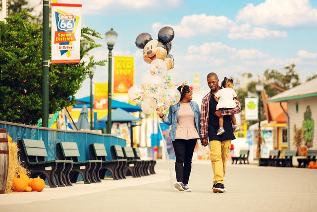 Family of three walking with Micky Mouse balloons at a theme park in Orlando, Florida. 