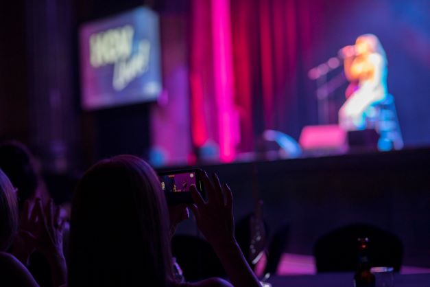 Close up, fan taking picture on phone, Carly Pearce on stage in distance, HGV Live!, Hard Rock Orlando, Florida. 