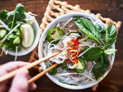 A hand holds chopsticks over a bowl of pho beef noodle soup