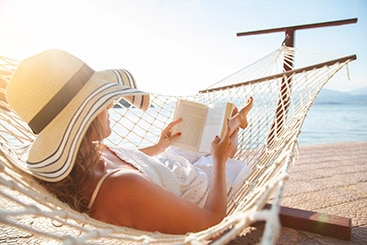 Woman reading a book while relaxing in a hammock on the beach.